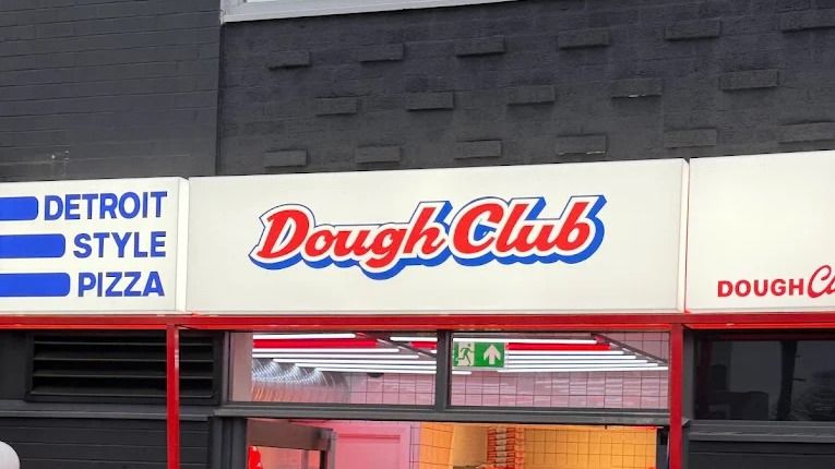 The Dough Club fascia at Metropolitan House on Station Road in Cheadle Hulme, the Dough Club wordmark in red on white beside a panel reading Detroit Style Pizza, above the shop entrance.