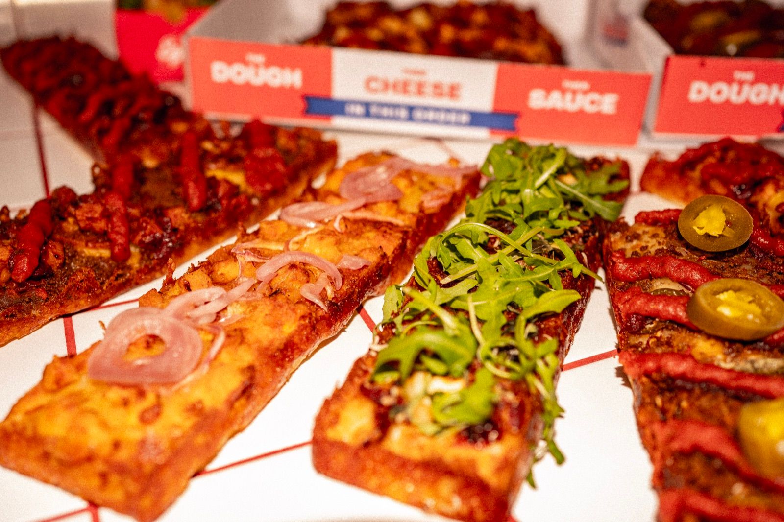 A row of Dough Club slices seen from the side, each with a dark caramelised cheese edge