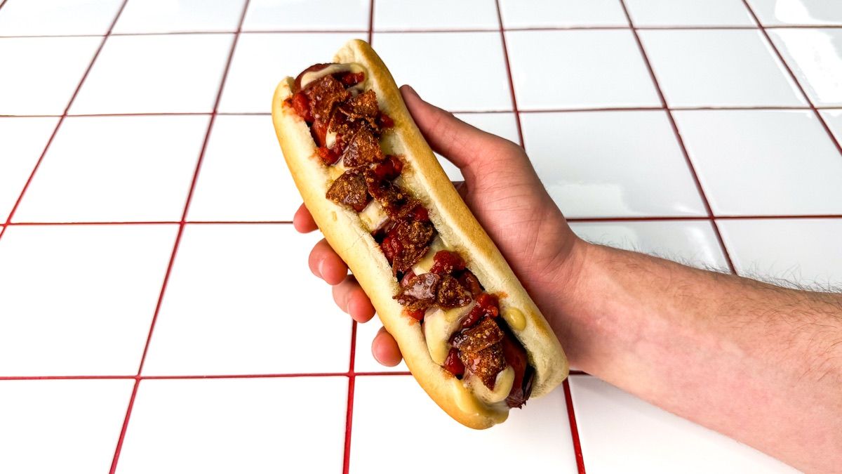 A Dough Club Hot Honey spiral hot dog, cheddar sauce, pizza sauce and pepperoni crumb, held in one hand