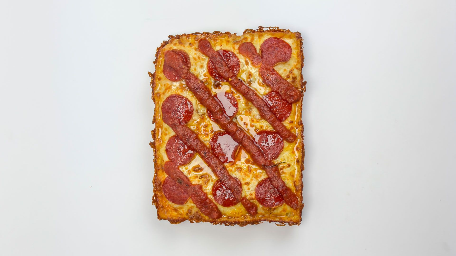A Dough Club Sweet Peps pan pizza from above, pepperoni under diagonal lines of hot honey